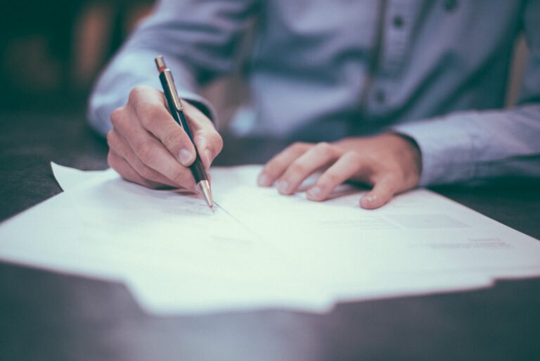 Mãos assinando documentos sobre uma mesa
